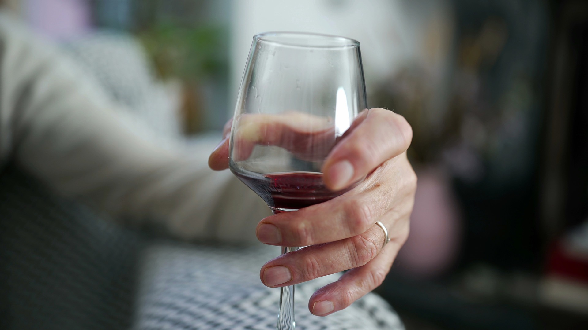 Äldre person sitter i en soffa med ett glas rött vin i handen.