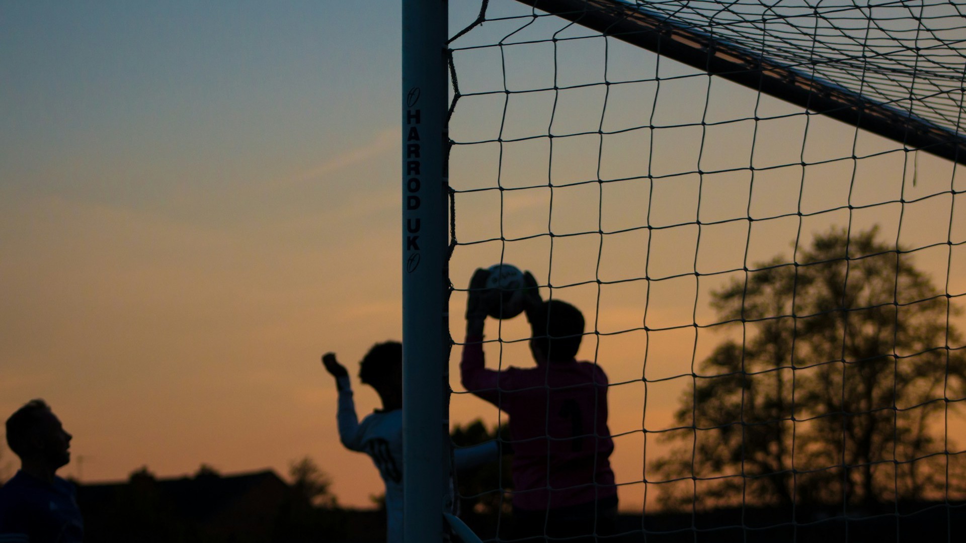 Barn spelar fotboll i skymningen.